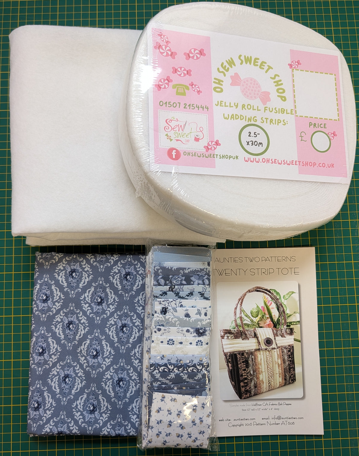 A sewing pattern kit from On Semi Sweet Shop on a green cutting mat, containing white fabric, a roll of white wedding strips, two packaged blue and white patterned fabric strips, and a printed pattern booklet.