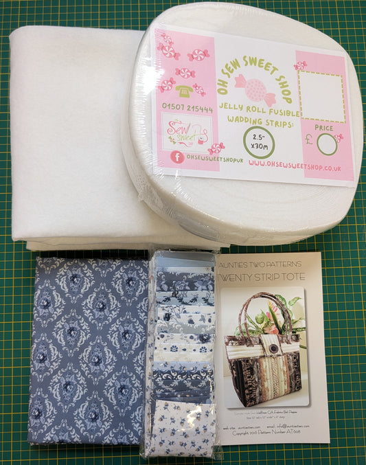 A sewing pattern kit from On Semi Sweet Shop on a green cutting mat, containing white fabric, a roll of white wedding strips, two packaged blue and white patterned fabric strips, and a printed pattern booklet.